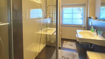 Ein modernes Badezimmer mit Duschkabine aus Glas, Waschbecken und Fenster.