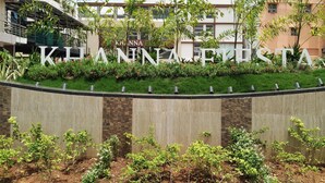 Un área ajardinada con un letrero que dice 'KHANNA FIESTA' y un edificio al fondo.