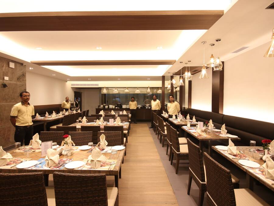 Un restaurante con varias mesas dispuestas, cubiertas con manteles y servilletas blancos, sillas de madera y lámparas colgantes.