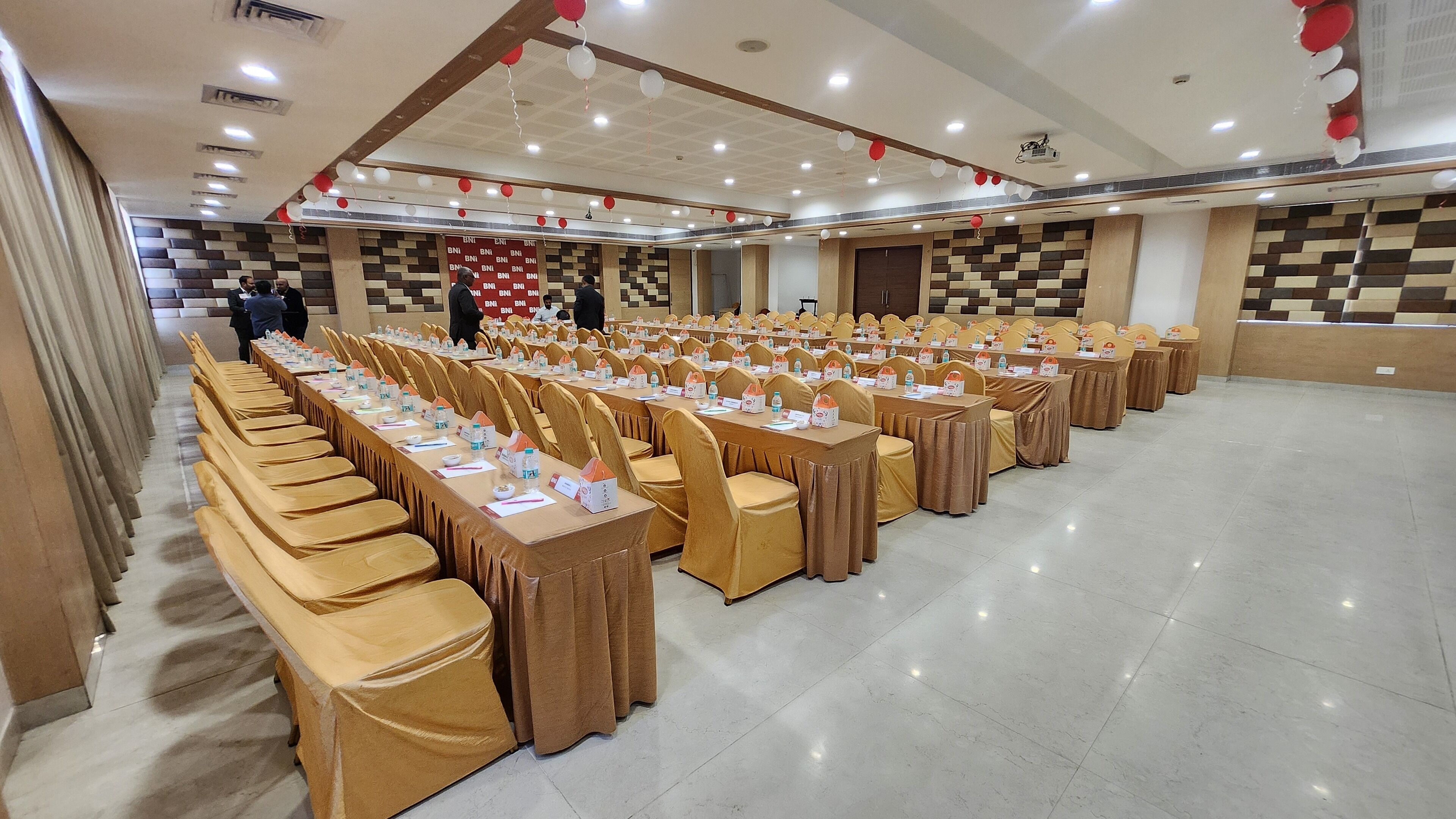 A conference room with rows of tables and chairs, a stage with a podium, and a patterned wall.