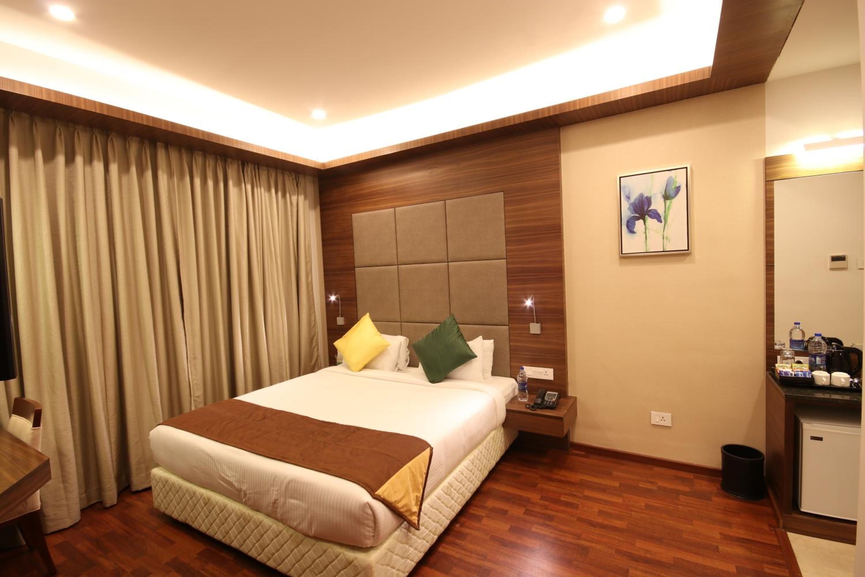 Quarto de hotel com uma cama grande, cabeceira de madeira, mesa de cabeceira, escrivaninha e uma pequena cozinha compacta.