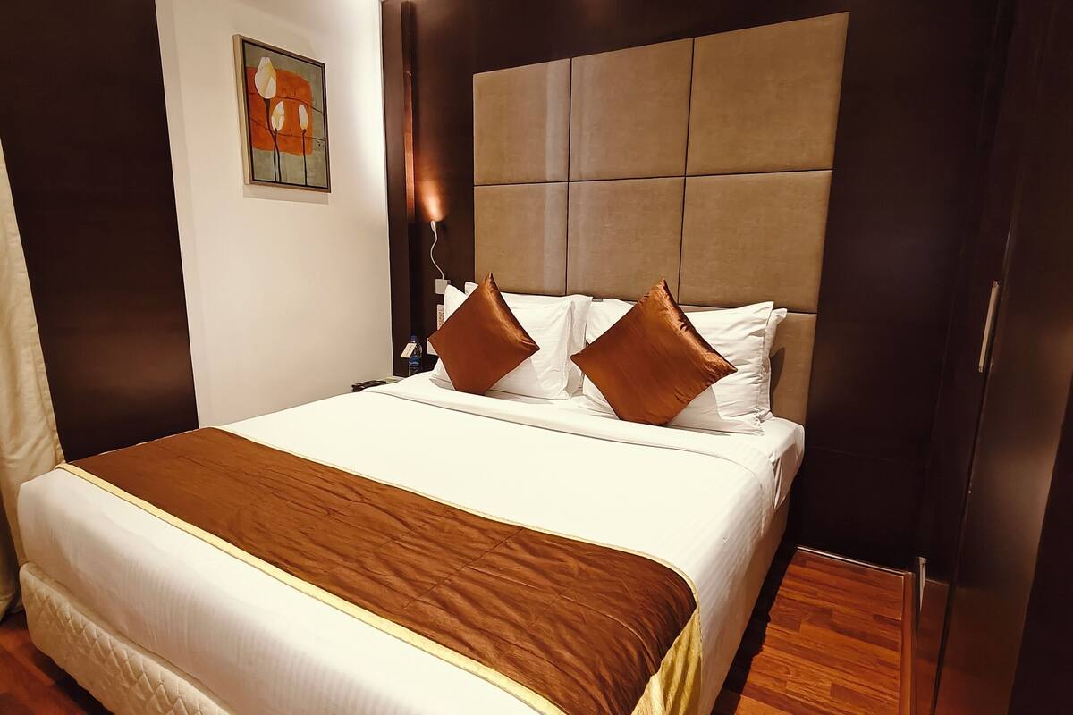 A hotel room with a large bed, a headboard with a padded panel, and a painting on the wall.