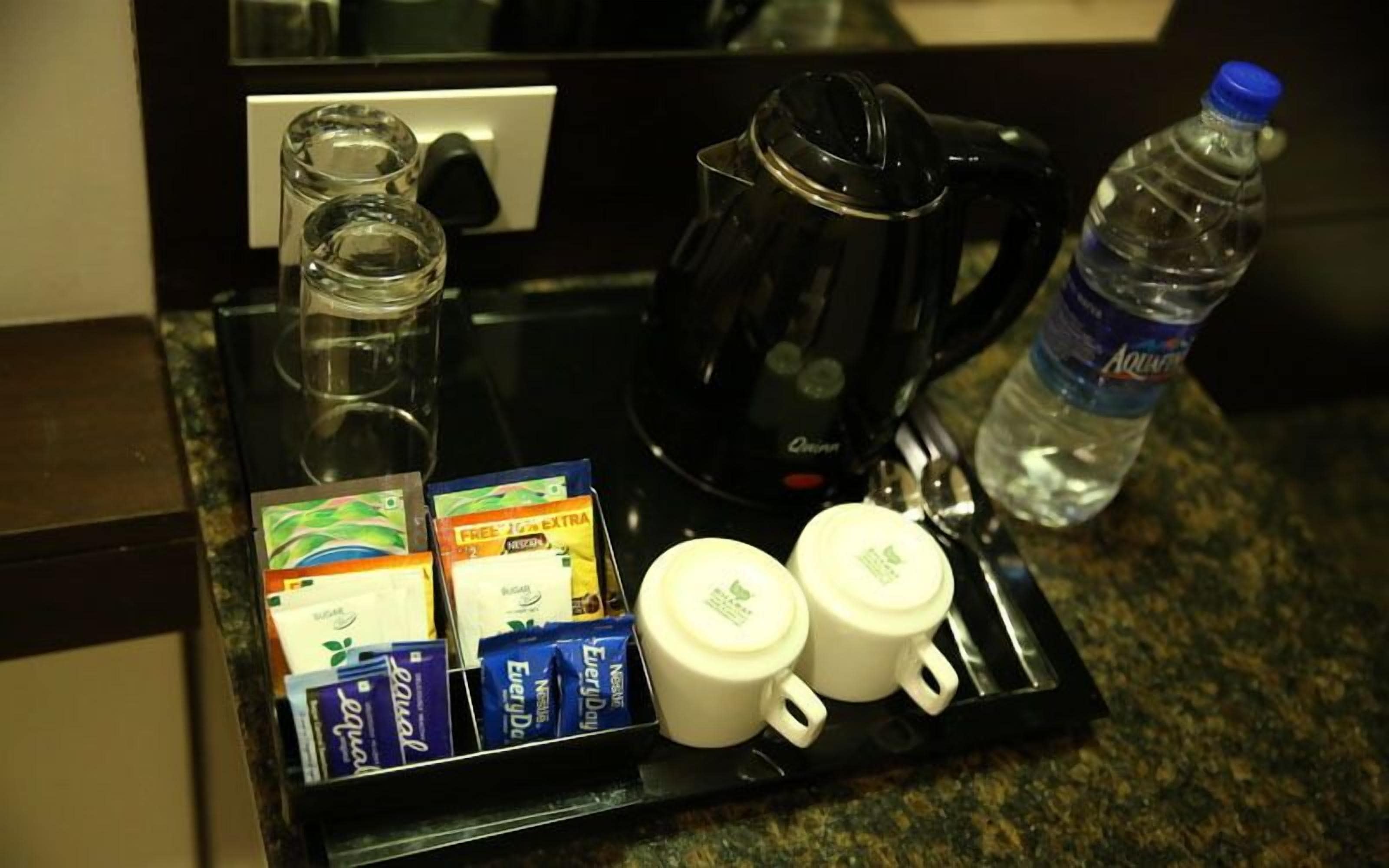 A breakfast tray with coffee maker, water bottle, sugar packets, and coffee cups.