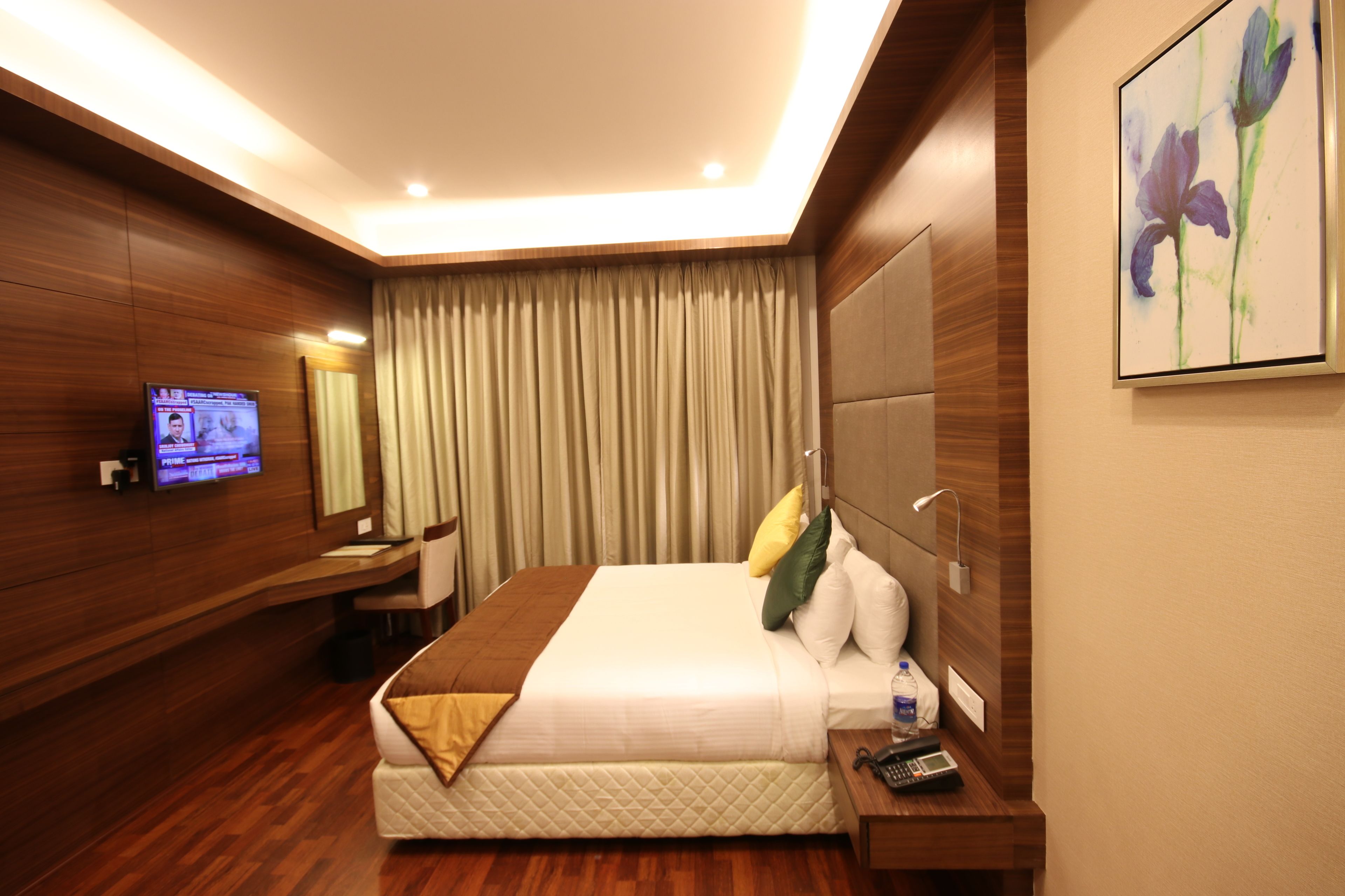 Habitación de hotel con una cama grande, un televisor montado en la pared, un escritorio con una silla y un cuadro en la pared.