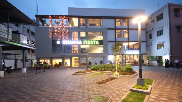 Un edificio con un letrero que dice "KHANNA FIESTA" y un patio empedrado con macetas y un farol.