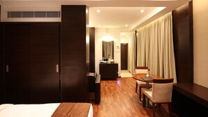 Habitación de hotel con cama, escritorio con silla, una mesita con otra silla y un ventanal con cortinas.