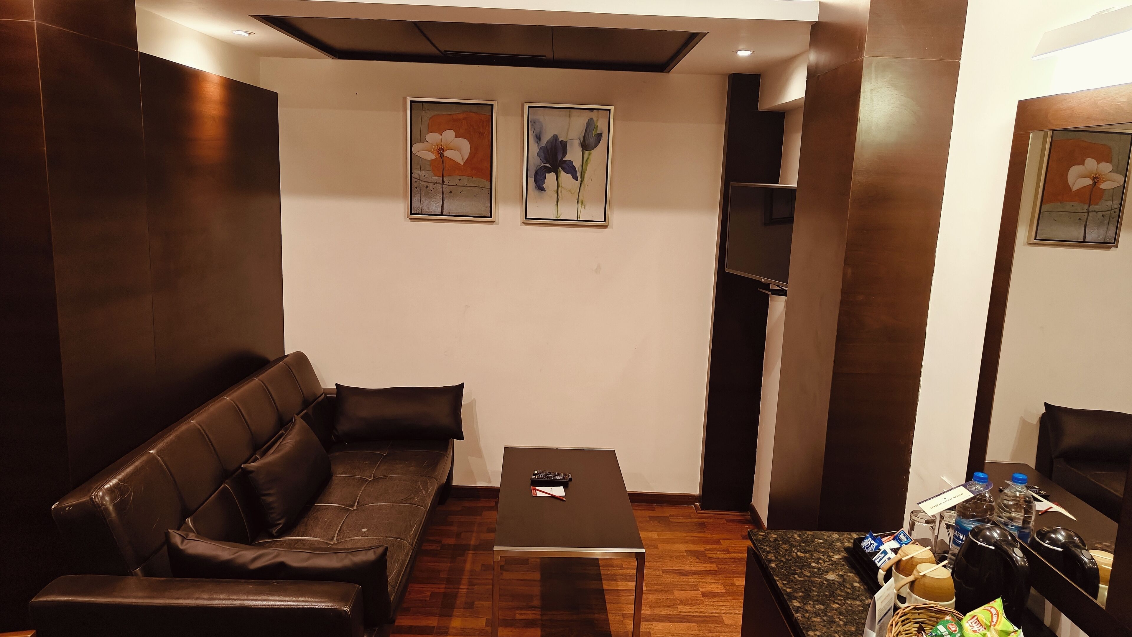 Una sala de estar con un sofá de cuero marrón, una mesa de centro negra y dos cuadros enmarcados con motivos florales en la pared.