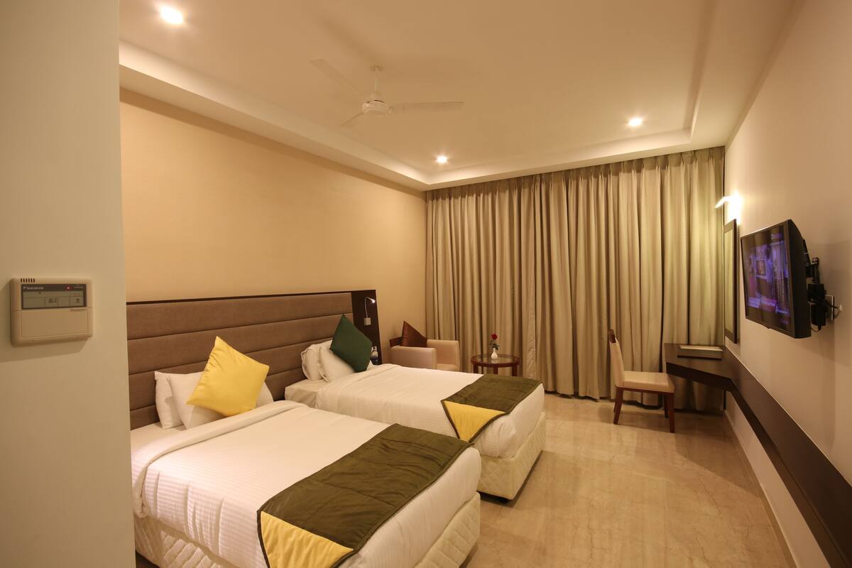 A hotel room with two beds, a ceiling fan, a TV, and a small table with a chair.