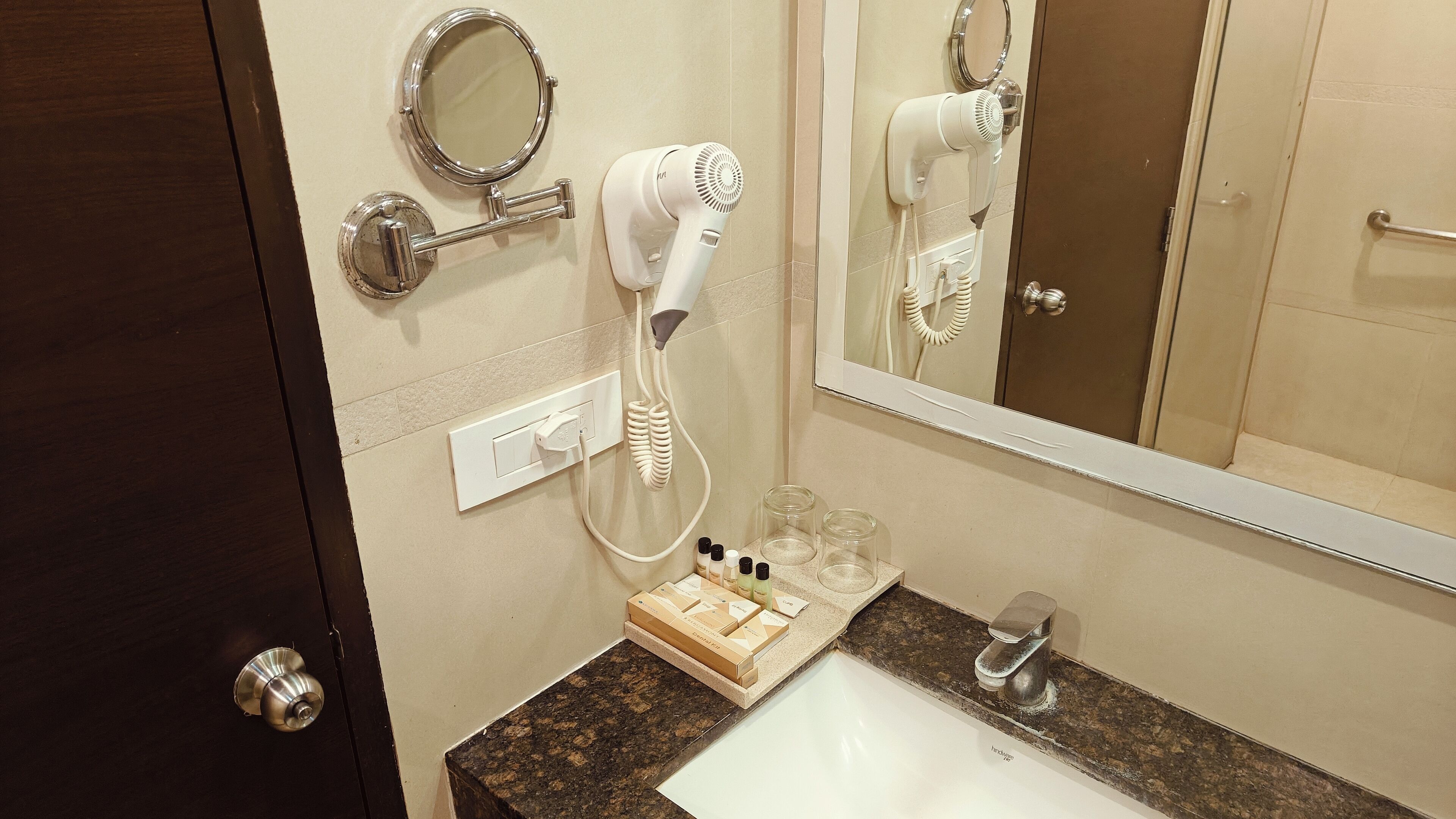 A bathroom with a sink, mirror, hairdryer, and toiletries.