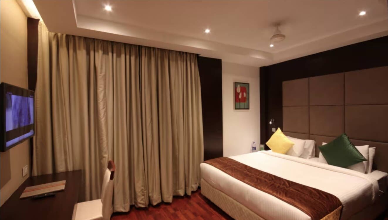 A hotel room with a large bed, a flat-screen TV, a desk, and a large window with curtains.
