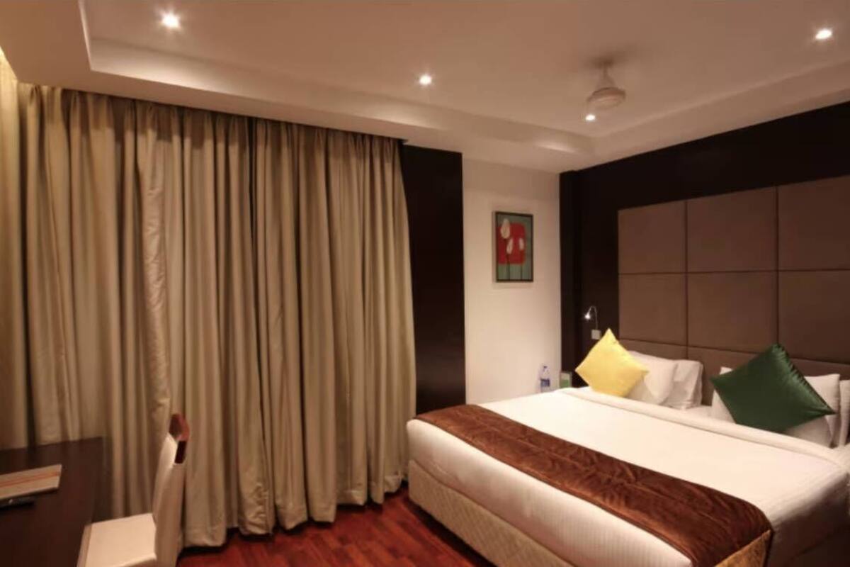 A hotel room with a large bed, a flat-screen TV, a desk, and a large window with curtains.