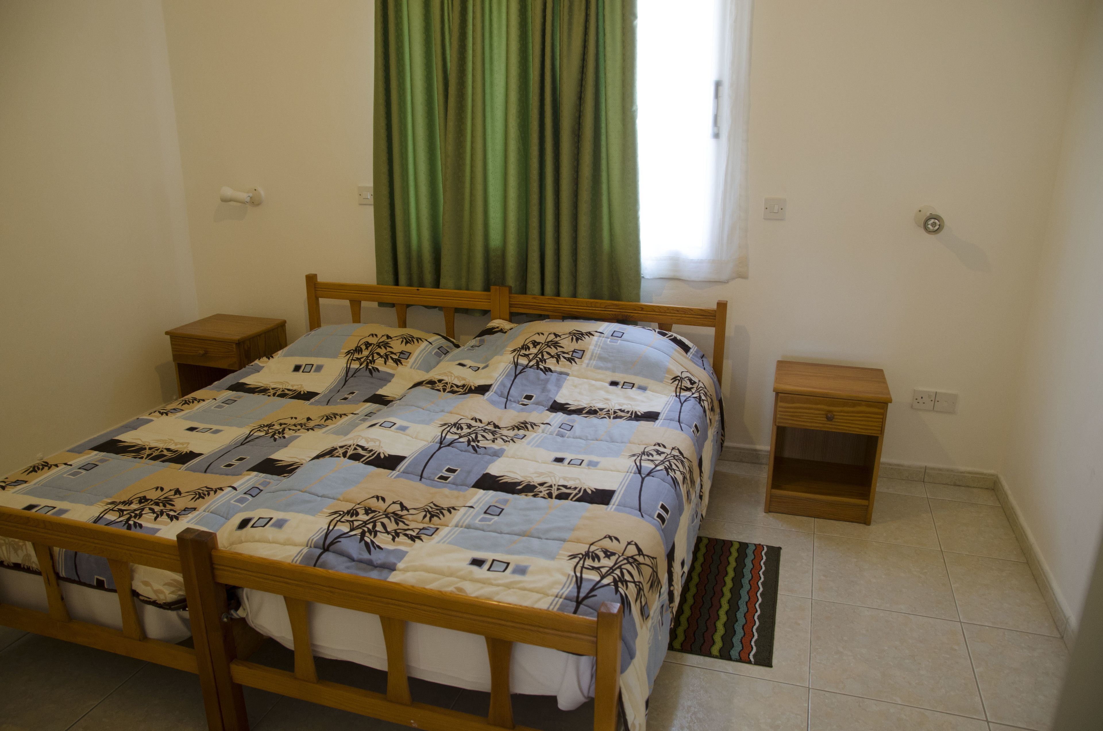 A bedroom with a wooden bed, two bedside tables, a green curtain, and a patterned rug.