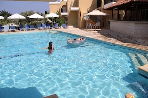 Ein Schwimmbecken mit Liegestühlen und Sonnenschirmen, umgeben von Gebäuden mit Balkonen.
