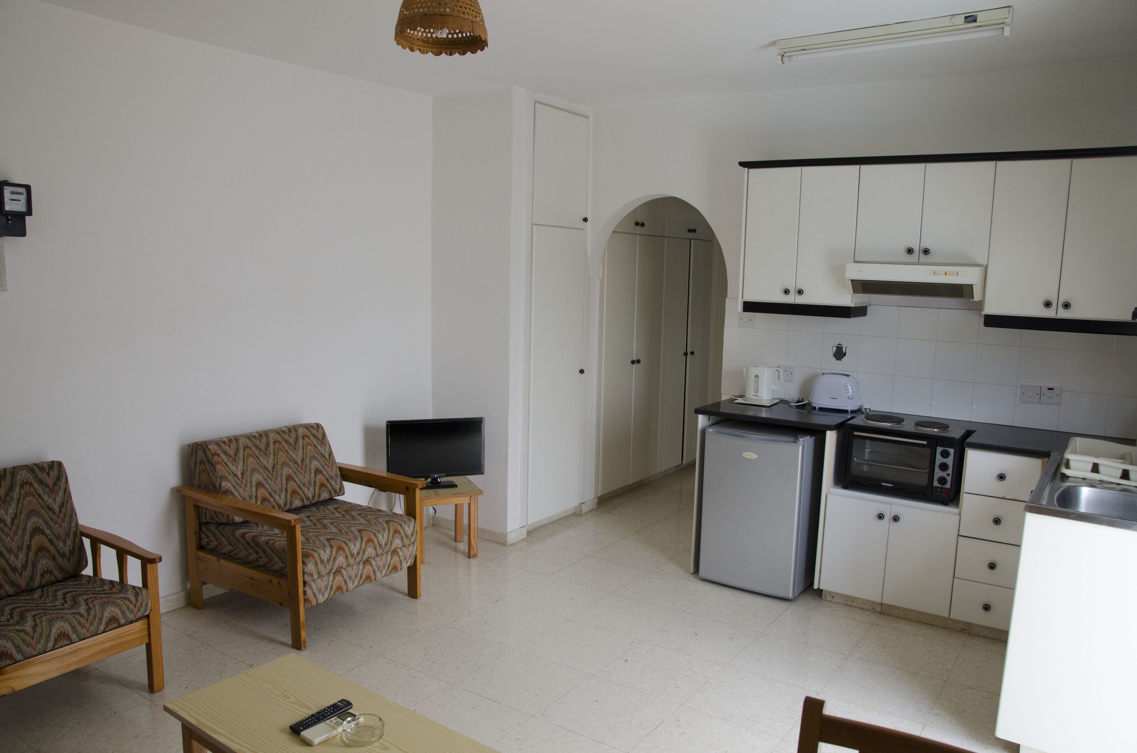 Un espacio habitable compacto con kitchenette, una zona de comedor con mesa y sillas, y un televisor sobre un pequeño mueble.
