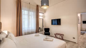 Ein Hotelzimmer mit Bett, Sessel, Wandfernseher und einer Tür zu einem weiteren Raum.