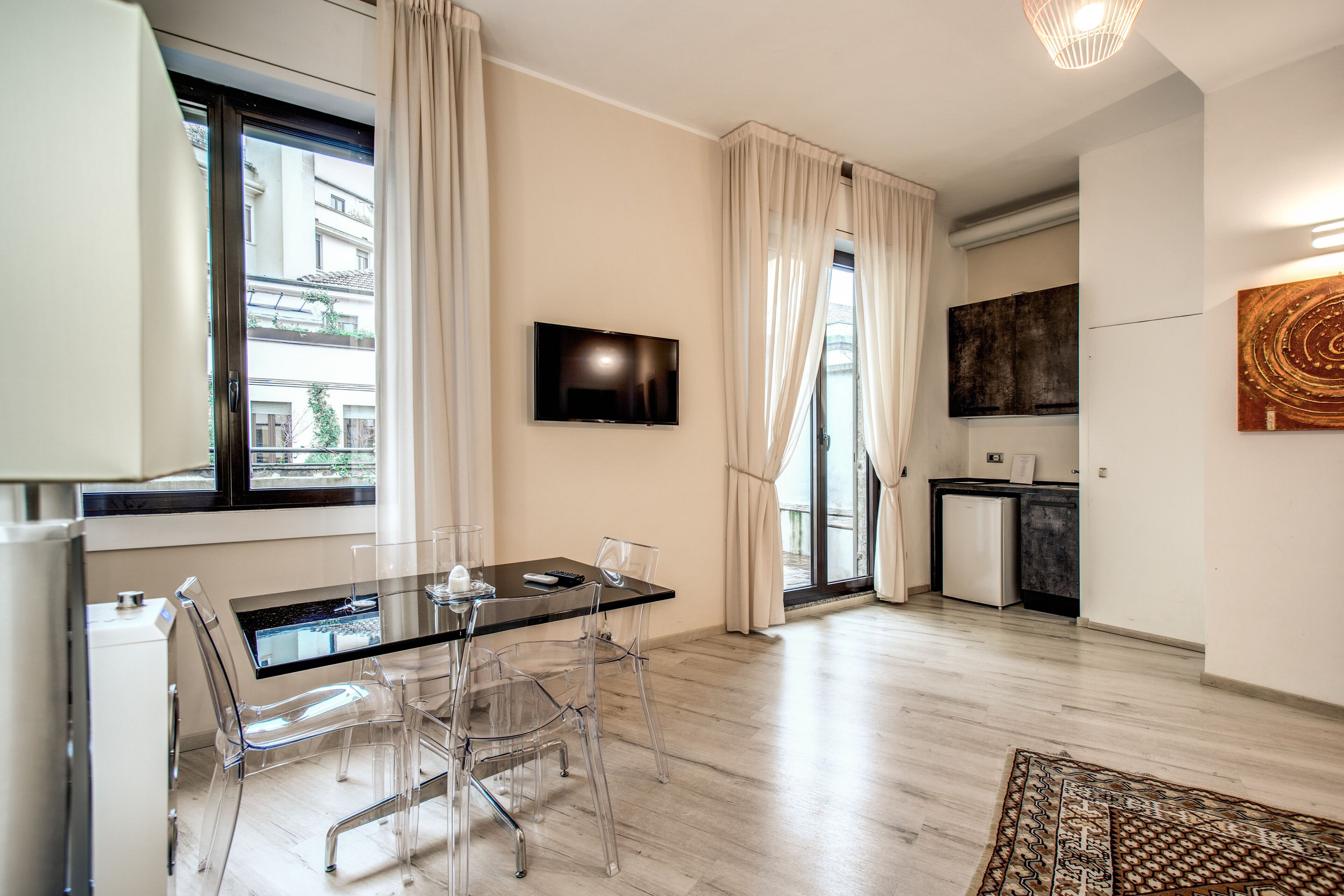 Une cuisine moderne dotée d’un téléviseur à écran plat, d’un coin repas avec une table et des chaises en verre, et offrant une vue sur la ville grâce à de grandes fenêtres.
