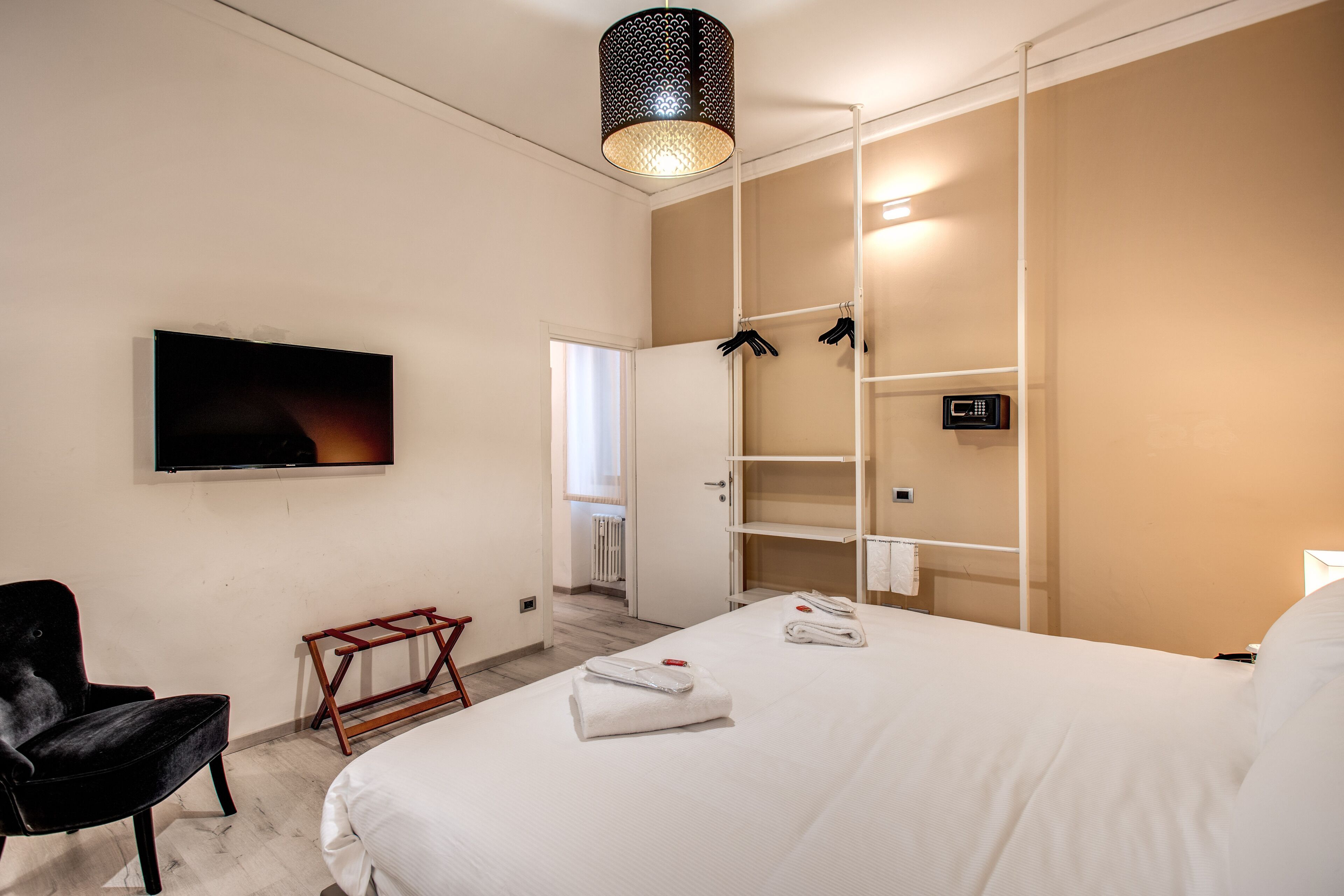 A hotel room with a bed, a TV, a chair, and a wardrobe.