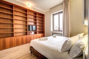 A bedroom with a large bed, a wooden built-in bookshelf, a television, and a window with curtains. - Suite Santa Tecla (Milan)