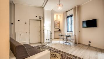 Ein modernes Wohnzimmer mit Sofa, einem Esstisch mit Stühlen, einem an der Wand montierten Fernseher und einem gemusterten Teppich.