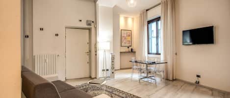 Un salon moderne avec un canapé, une table à manger et des chaises, un téléviseur fixé au mur et un tapis à motifs.