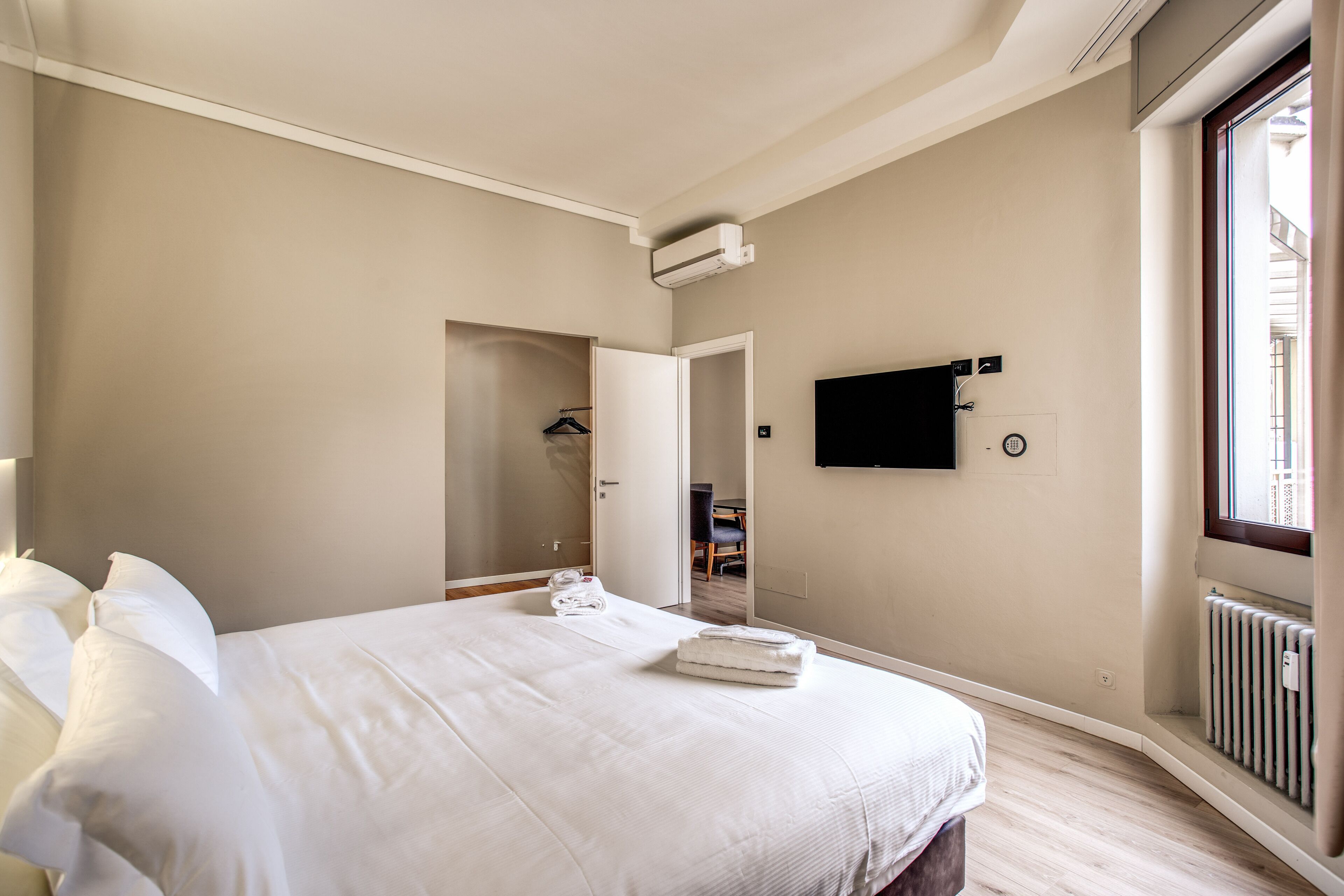 A bedroom with a bed, a TV mounted on the wall, and a window.