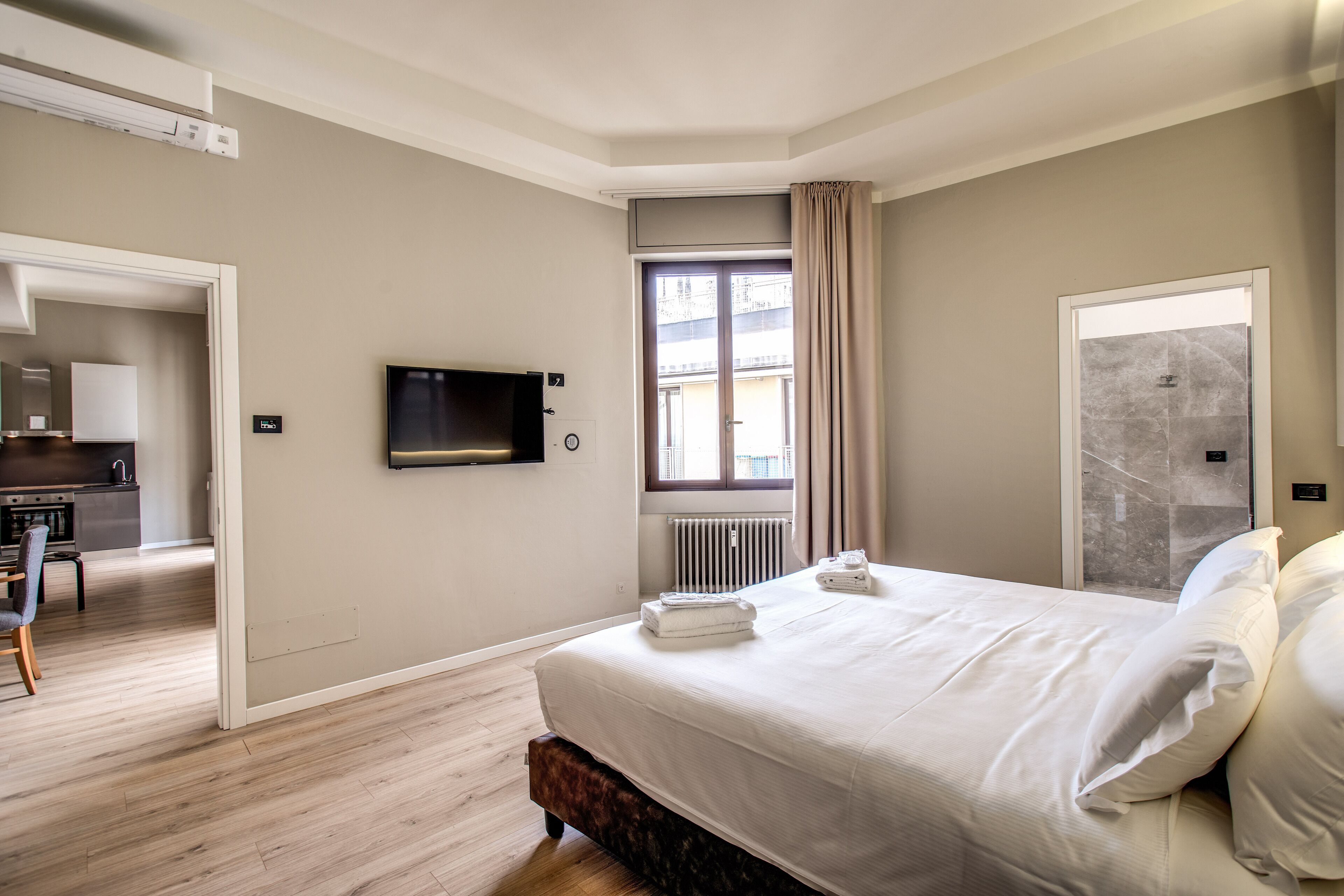 Una habitación de hotel con cama, televisión, ventana con cortinas, radiador y puerta.