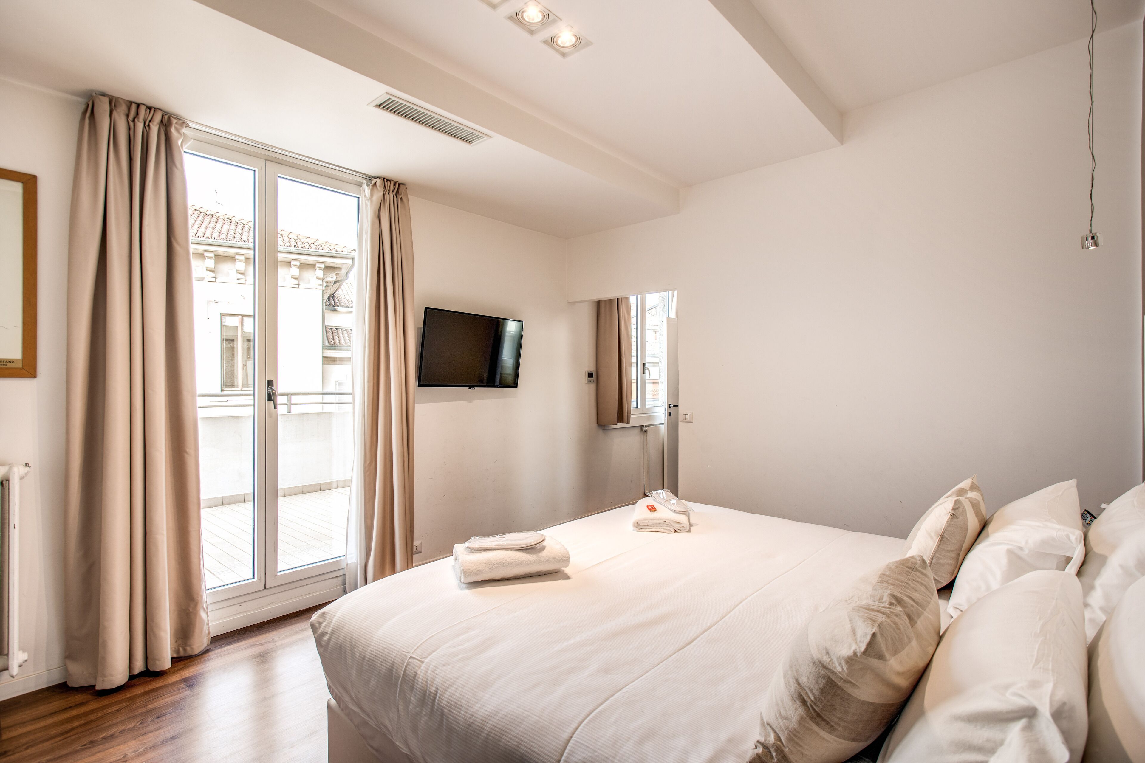 Habitación de hotel con una cama grande, un televisor de pantalla plana, una puerta corredera de vidrio al balcón y un televisor montado en la pared.