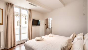Habitación de hotel con una cama grande, un televisor de pantalla plana, una puerta corredera de vidrio al balcón y un televisor montado en la pared.