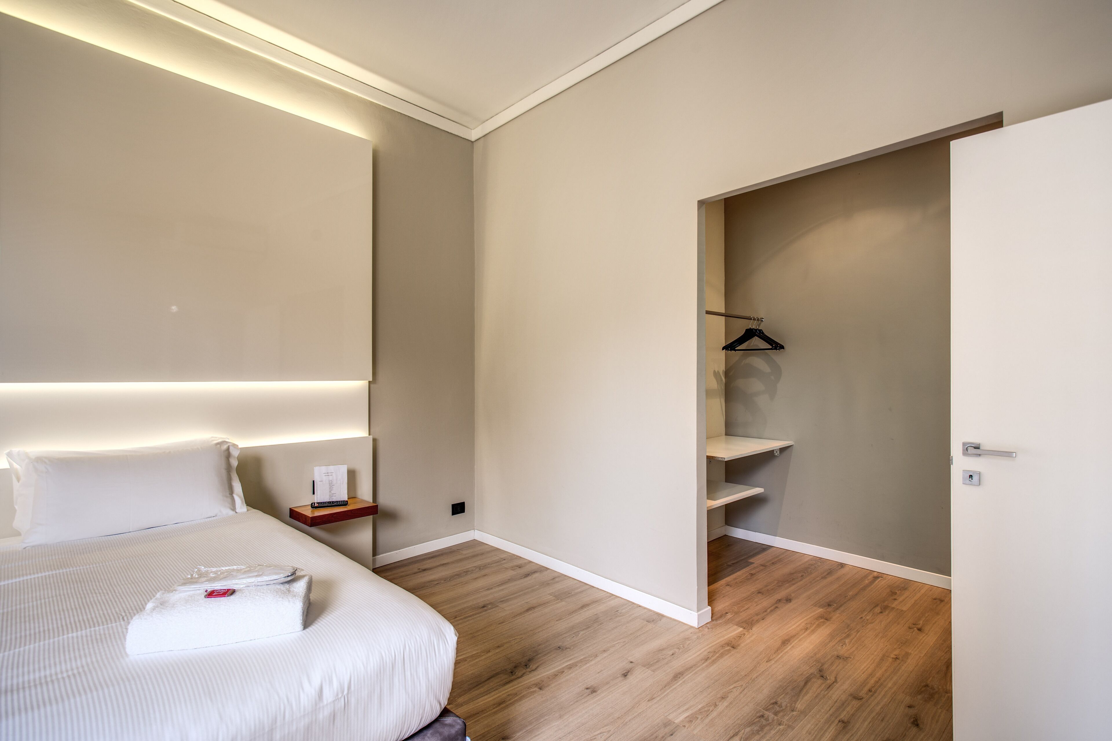 Ein Hotelzimmer mit einem ordentlich bezogenen Bett, einem Nachttisch mit Lampe und Holzboden.