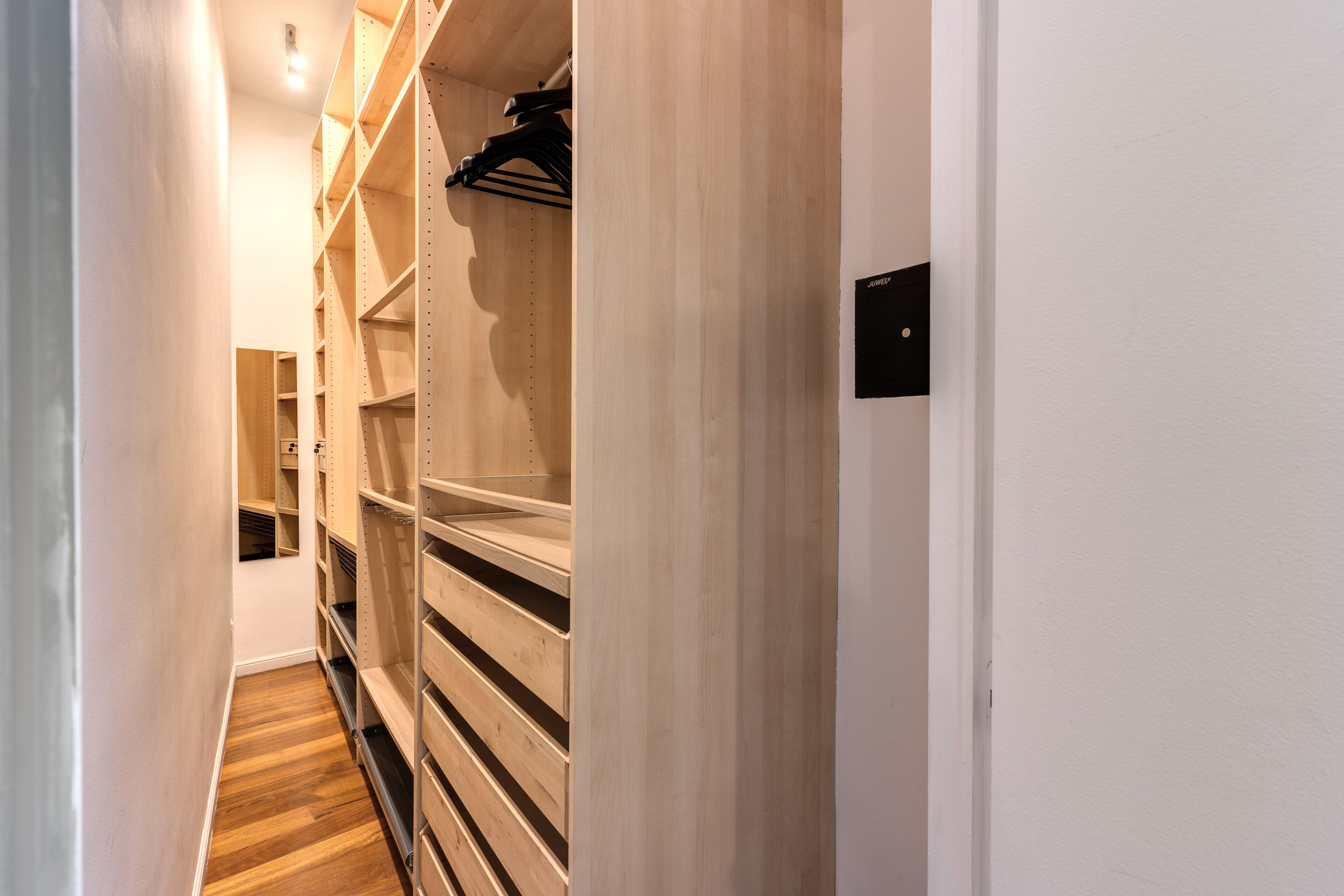 A narrow hallway with wooden shelving units and a black coat rack.