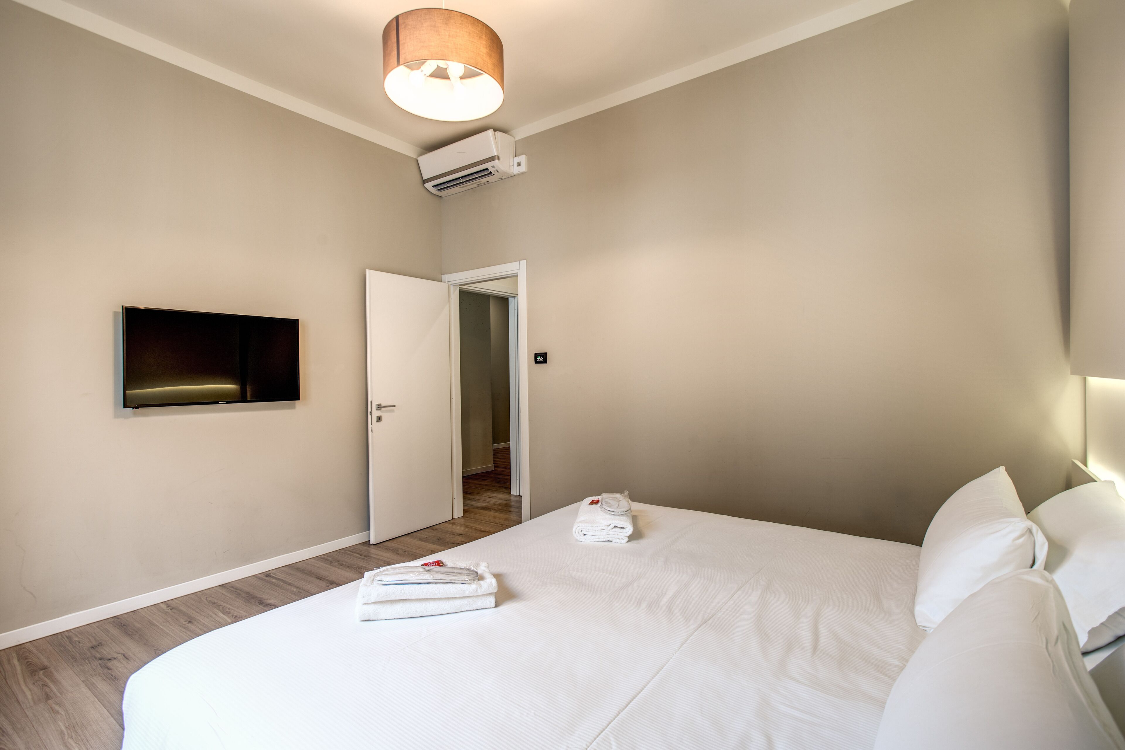 Quarto de hotel com uma cama grande, televisão de tela plana na parede, porta que dá para outro cômodo e ar-condicionado na parede.