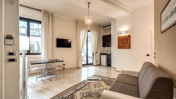 Uma sala de estar moderna com sofá, área de jantar com mesa e cadeiras de vidro, cozinha ao fundo e uma grande janela com cortinas.