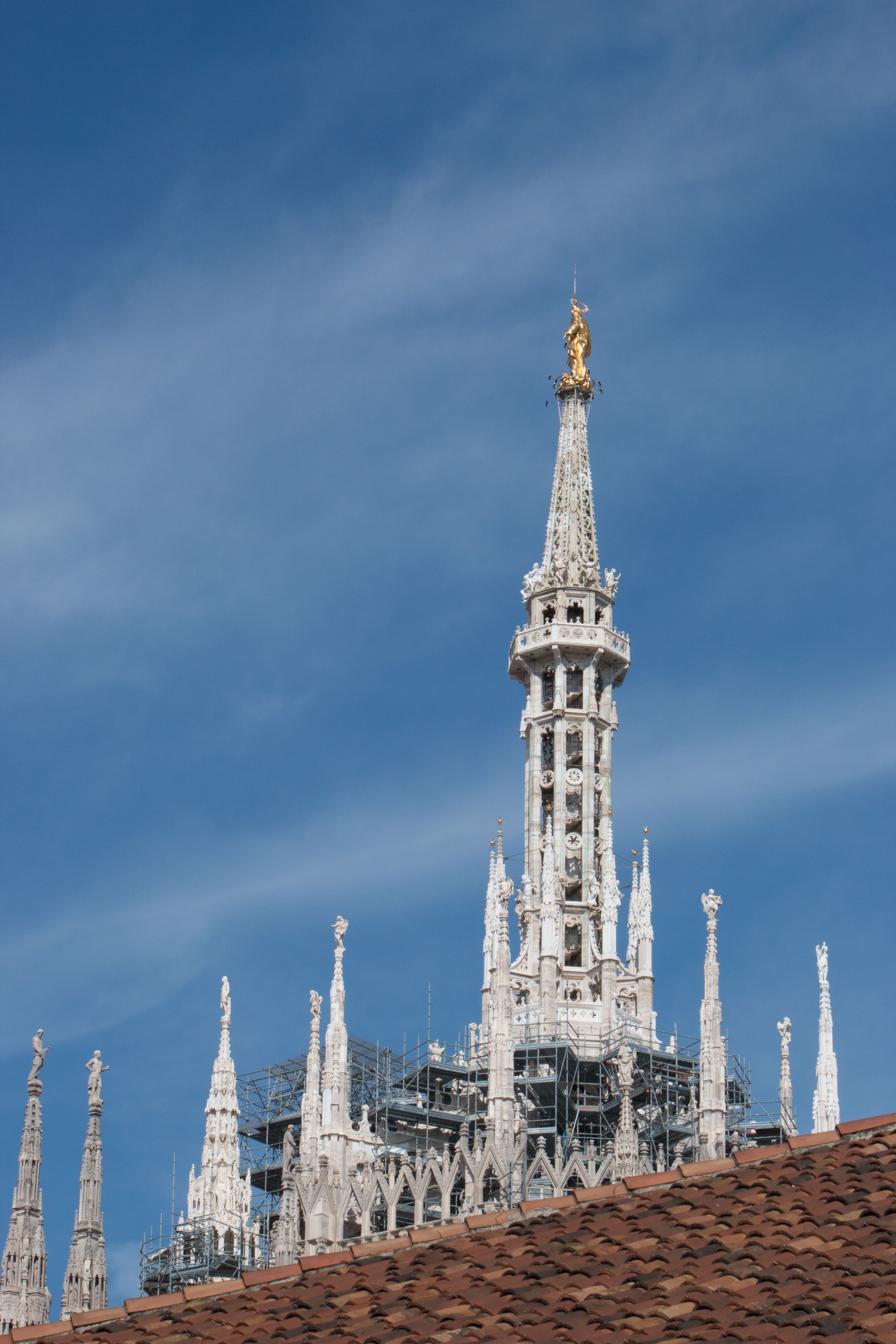 A Gothic-style cathedral with intricate spires and a golden statue on top, under construction with scaffolding.