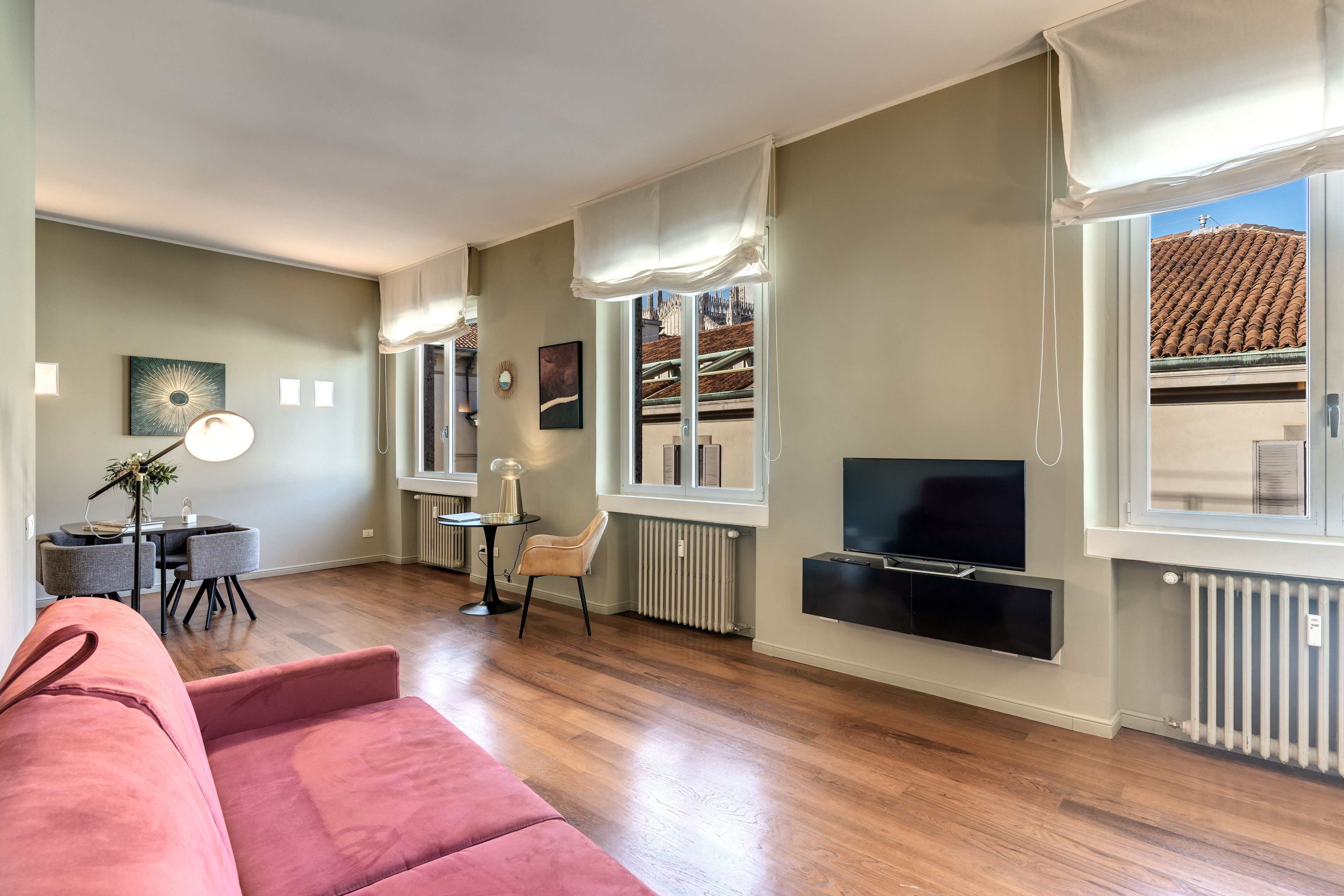 A modern living room with a sofa, a TV mounted on the wall, and a dining area with a table and chairs.