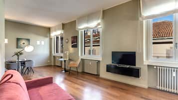 A modern living room with a sofa, a TV mounted on the wall, and a dining area with a table and chairs.