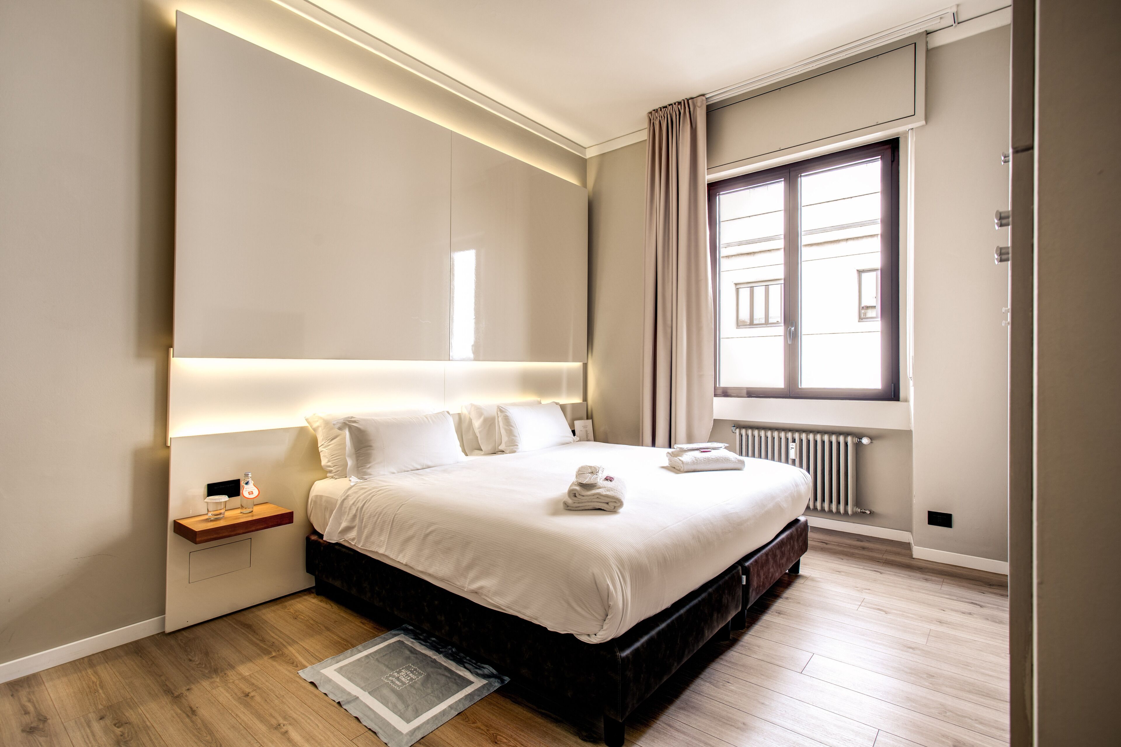 Una camera da letto moderna con un letto grande, comodini, un tavolino e una finestra con tende, più un termosifone.