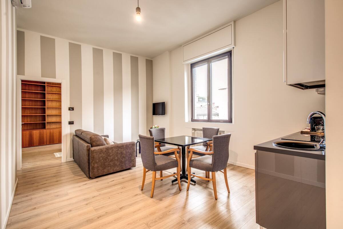 Un salon moderne comprenant un canapé, une table à manger avec des chaises, un téléviseur et un coin cuisine avec un évier et des placards.