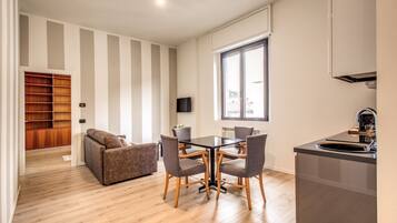 Uma sala de estar moderna com sofá, mesa de jantar com cadeiras, televisão e área de cozinha com pia e armários.