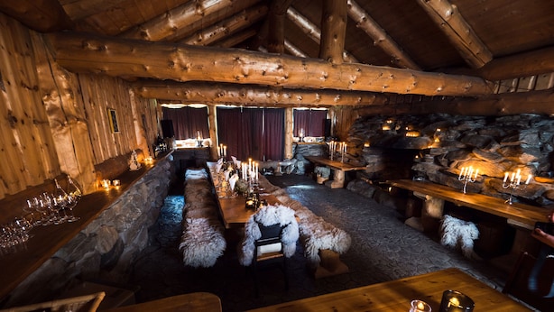 A rustic wooden interior with stone walls, a long dining table set for a meal, and candles on the tables. - Blåtind Boutique Hotel (Stordal)
