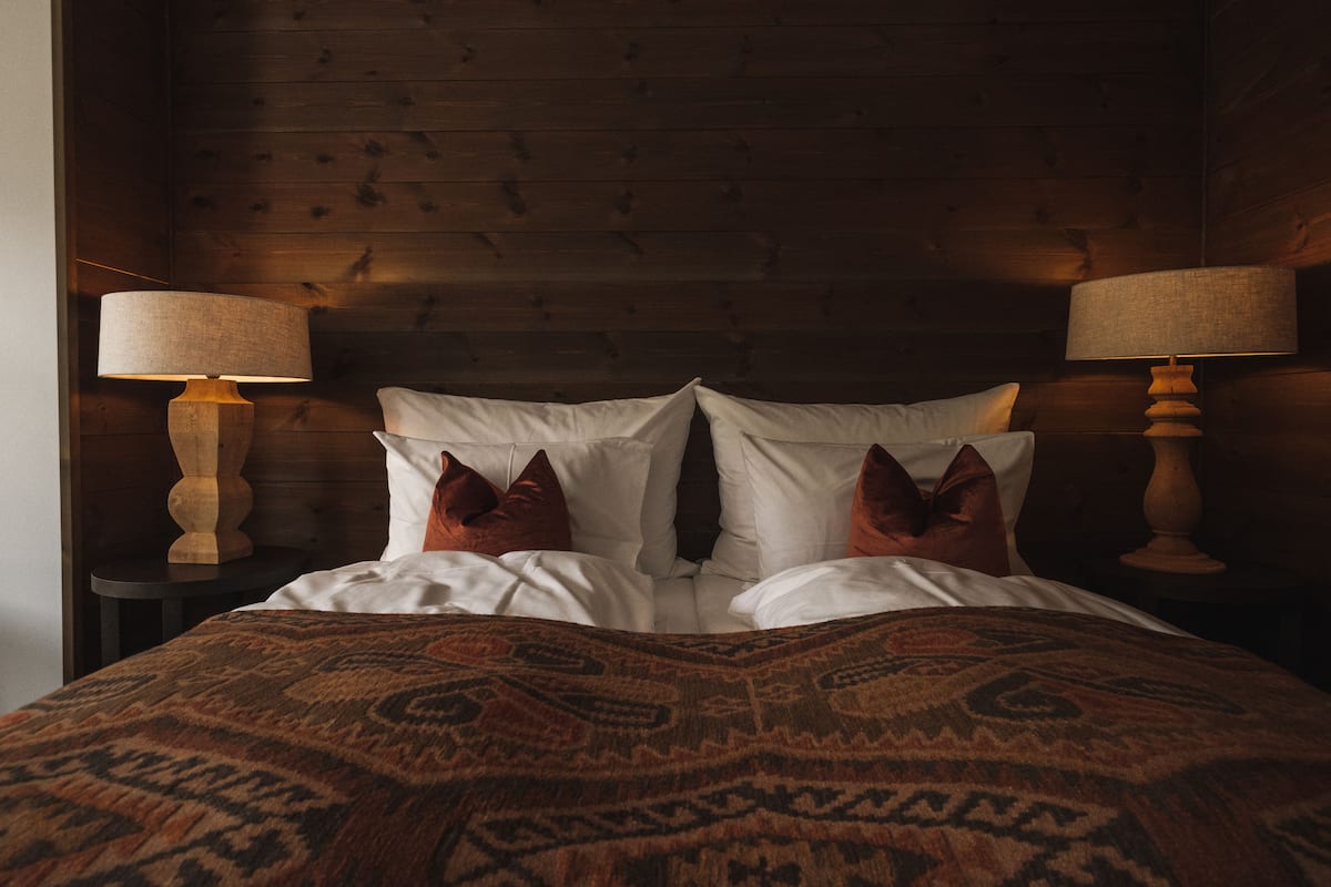 Een bed met witte lakens, een decoratief plaid en twee lampen aan weerszijden.