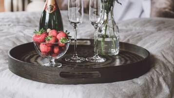 A tray with a bottle of champagne, a bowl of strawberries, and a vase with white flowers on a bed.