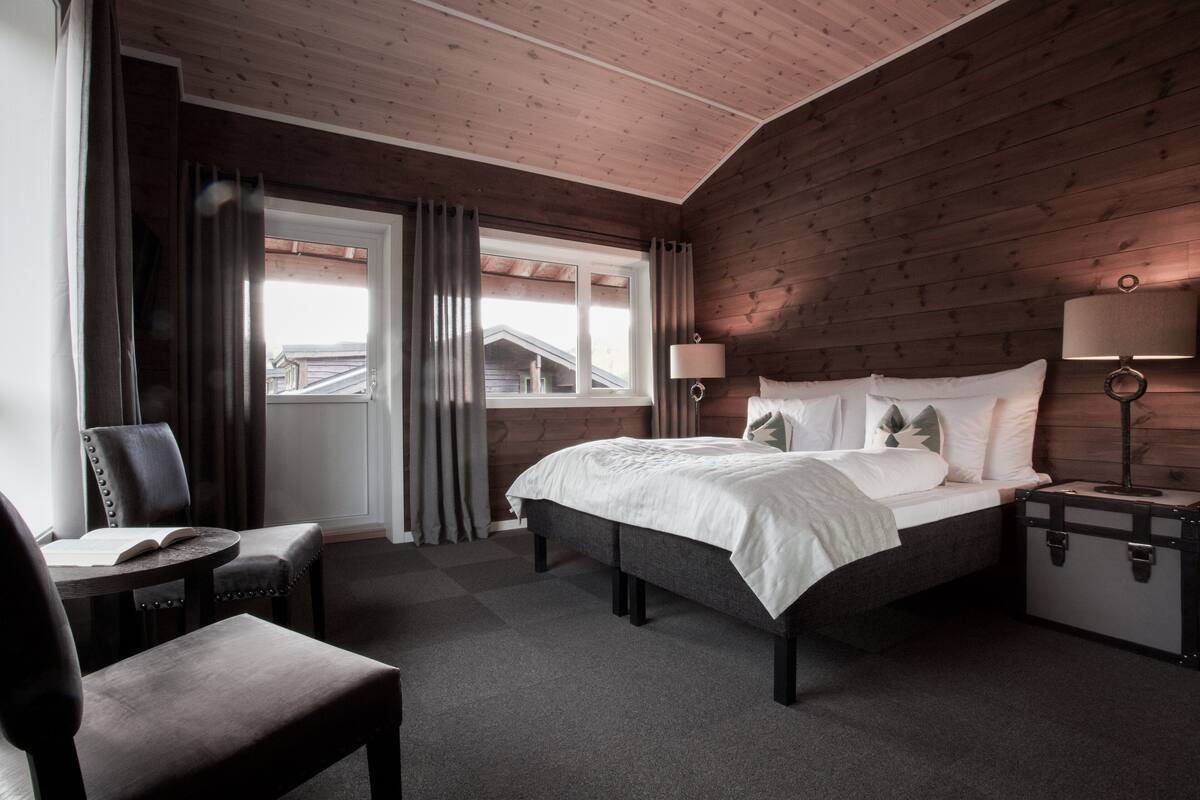 Een slaapkamer met houten lambrisering, een bed, bedlampen, een stoel, een tafel en een koffer.