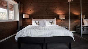 A bedroom with a wooden ceiling, a large bed with white bedding, two bedside lamps, and a suitcase on the floor. - Blåtind Boutique Hotel (Stordal)