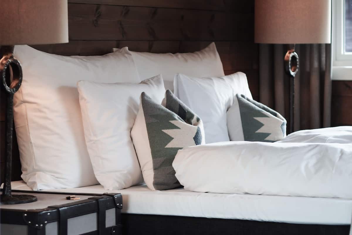 Een net opgemaakt bed met witte en gemêleerde kussens, een zwart hoofdbord en twee bedlampjes.