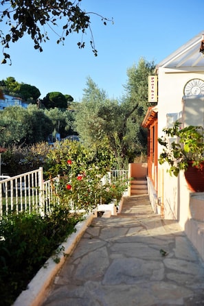 A stone pathway leading to a building with a clock and a sign that reads "Poolbar". - Marina Hotel (Skiathos)