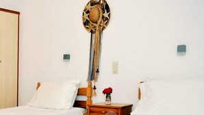 Ein Hotelzimmer mit zwei Betten, einem Holz-Kopfteil, einem Wandbild und einem Nachttisch mit einer Vase roter Blumen. Auf dem Bett liegt ein gerolltes Handtuch.