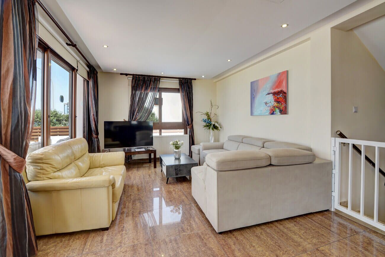A spacious living room with a leather sofa, a beige sofa, a flat-screen TV, and a painting on the wall.