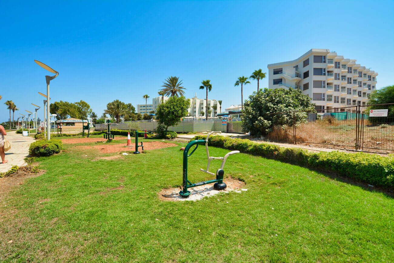 A well-maintained park with exercise equipment, a clear sky, and a modern building in the background.