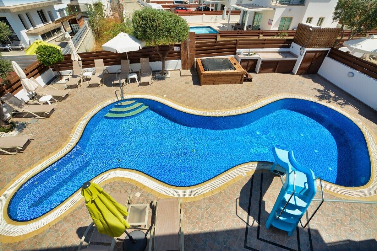 A swimming pool with a wavy edge, surrounded by lounge chairs and umbrellas.