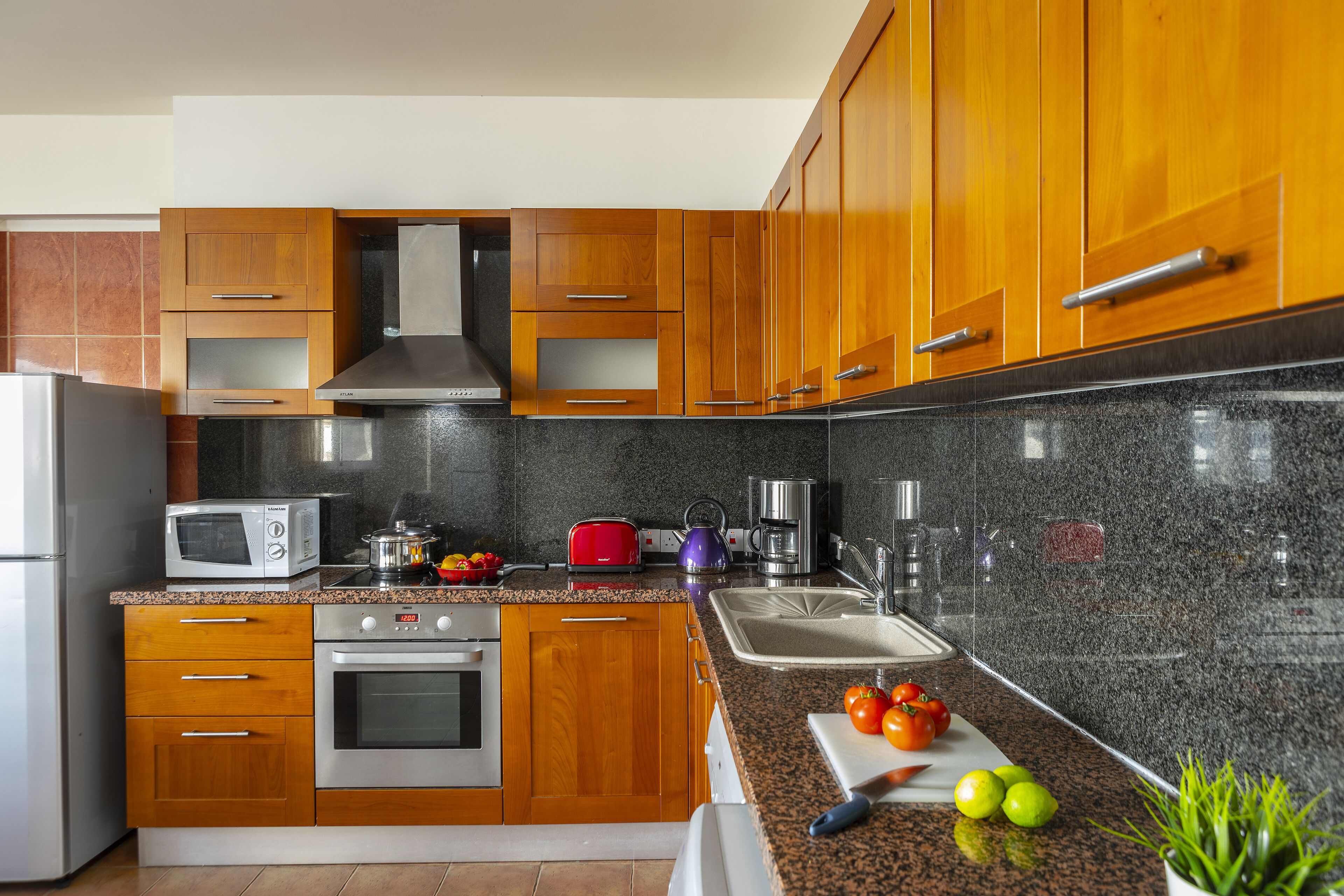 Una cocina moderna con armarios de madera, electrodomésticos de acero inoxidable, encimeras de granito y una variedad de utensilios y electrodomésticos.